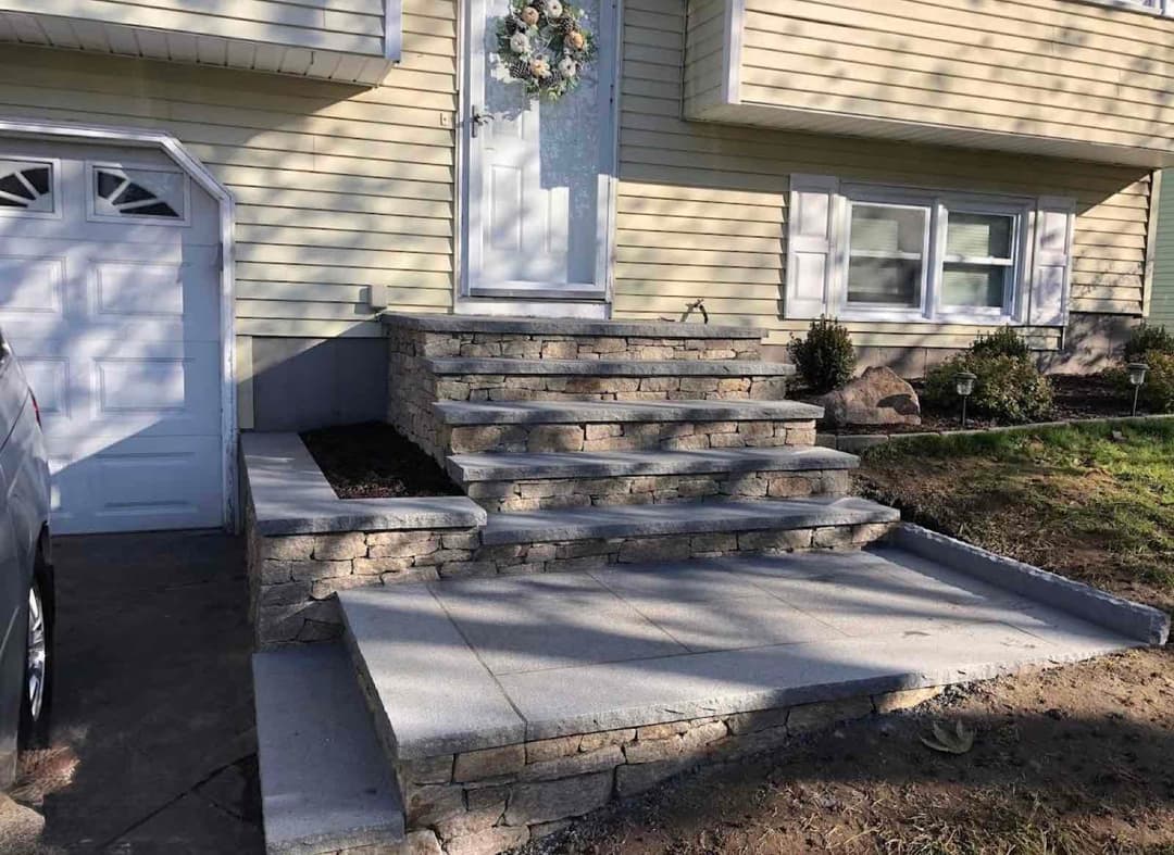Stone steps leading to a house entrance with a decorative wreath and landscaped surroundings.