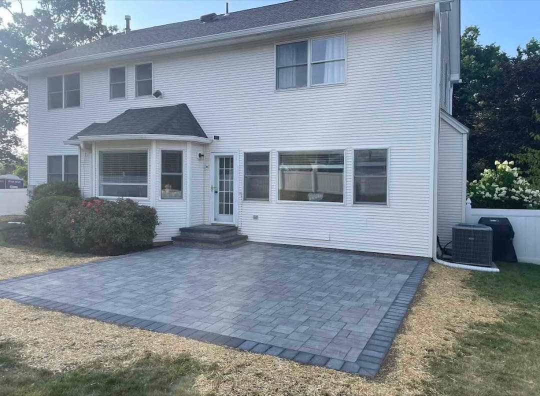 Modern home exterior with a paver patio, grass lawn, and landscaped bushes.