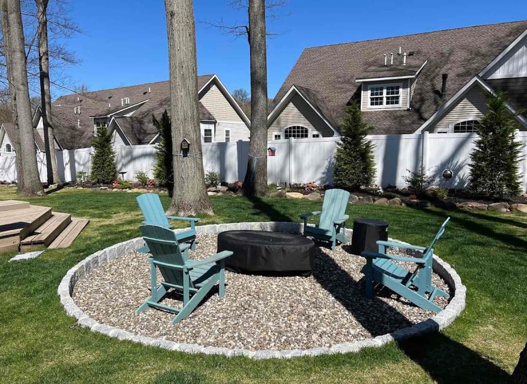 Cozy backyard fire pit area with blue Adirondack chairs and stone landscaping.