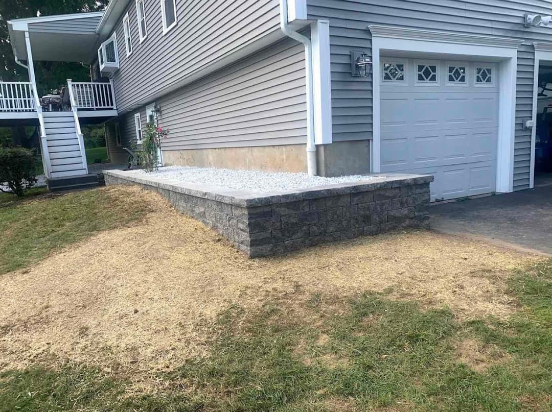 Landscape transformation featuring a stone retaining wall and gravel area beside a house.