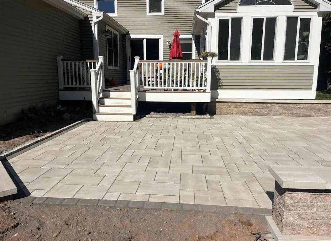 Paved outdoor patio with steps leading to a home, featuring a red umbrella and seating area.