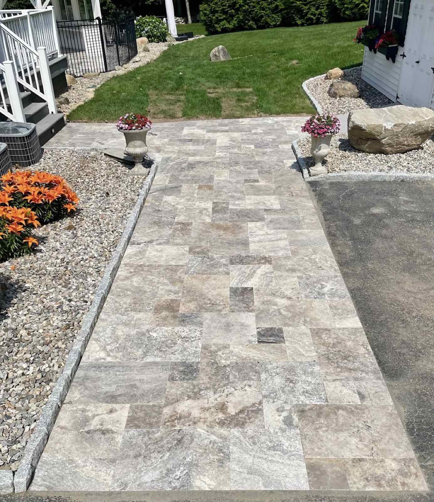 Paved walkway with stone patterns, bordered by flowers and decorative planters.