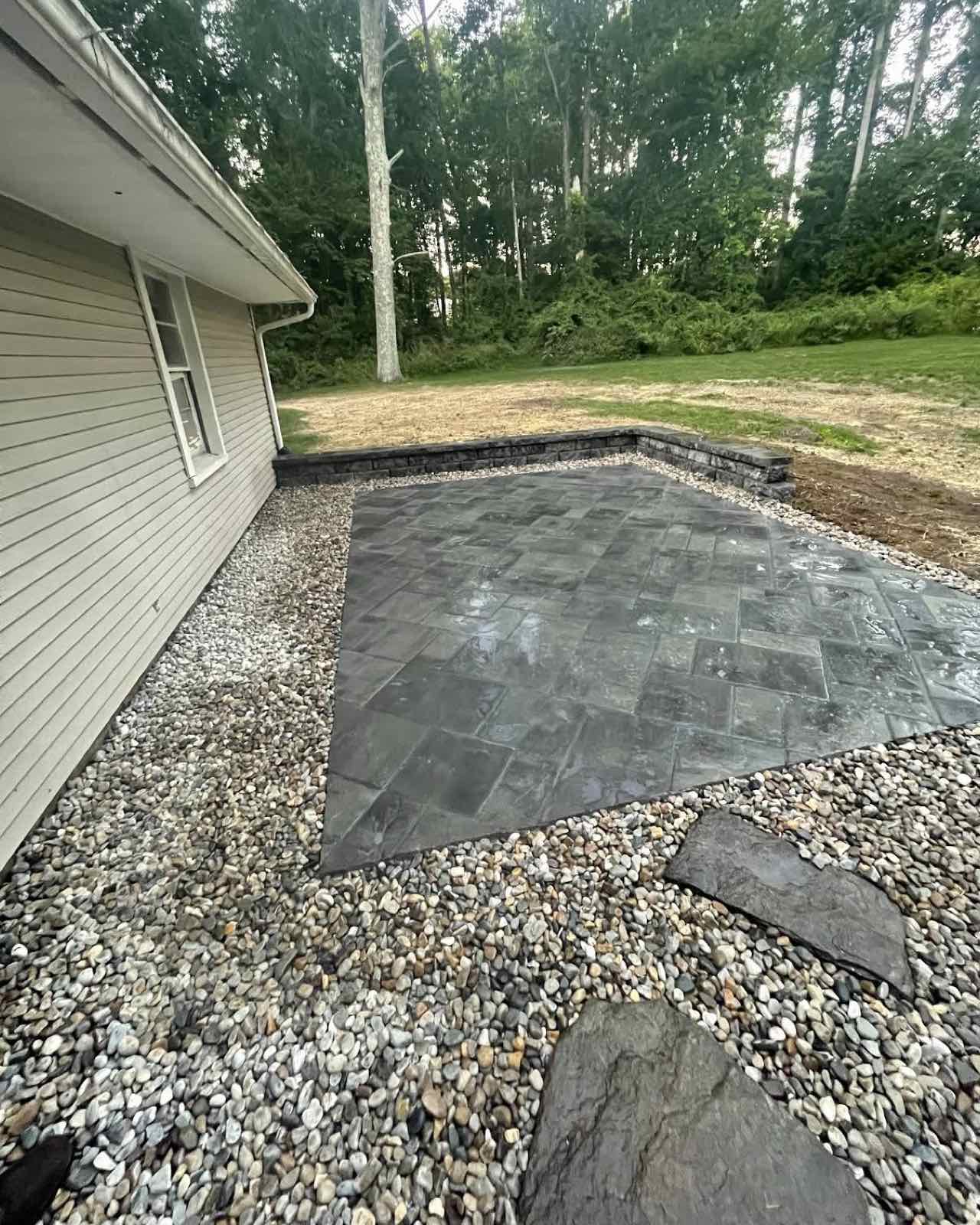 Patio with gray stone pavers and gravel detail next to house in wooded area.