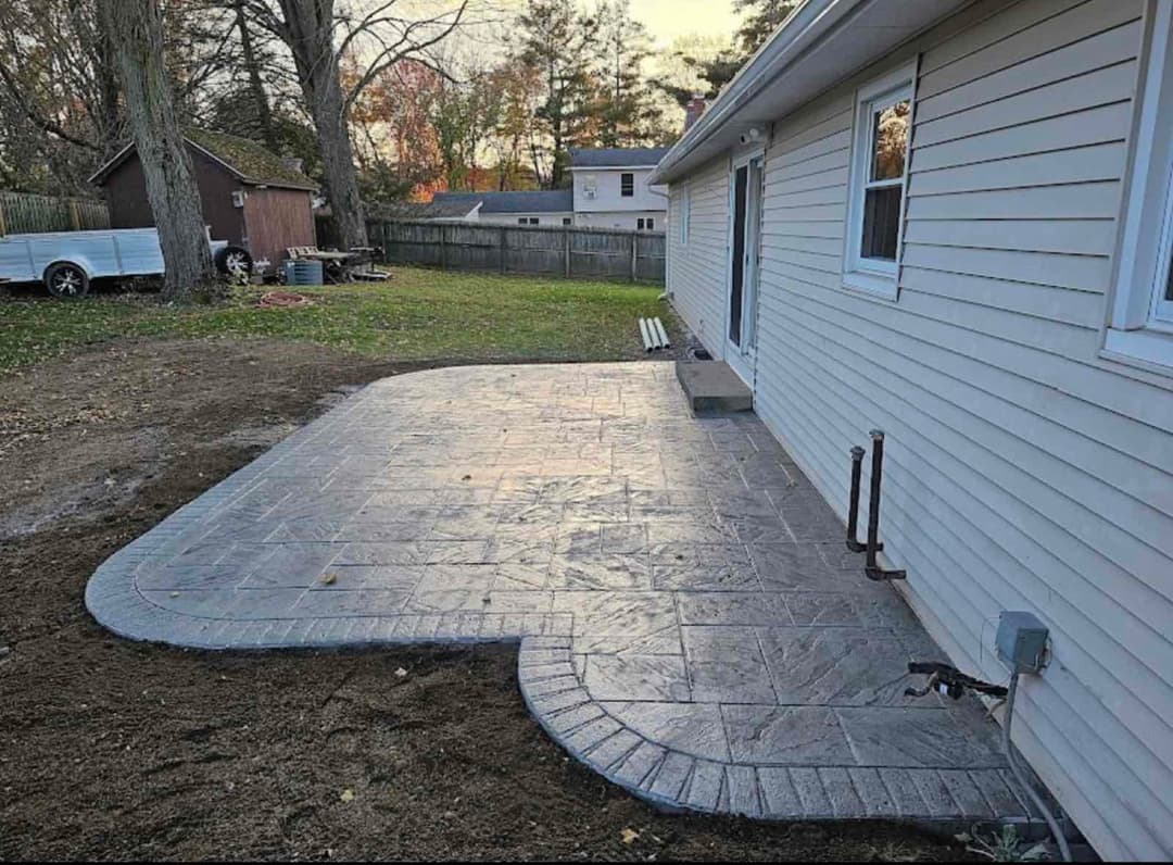 Newly installed stamped concrete patio next to a house with landscaped yard.
