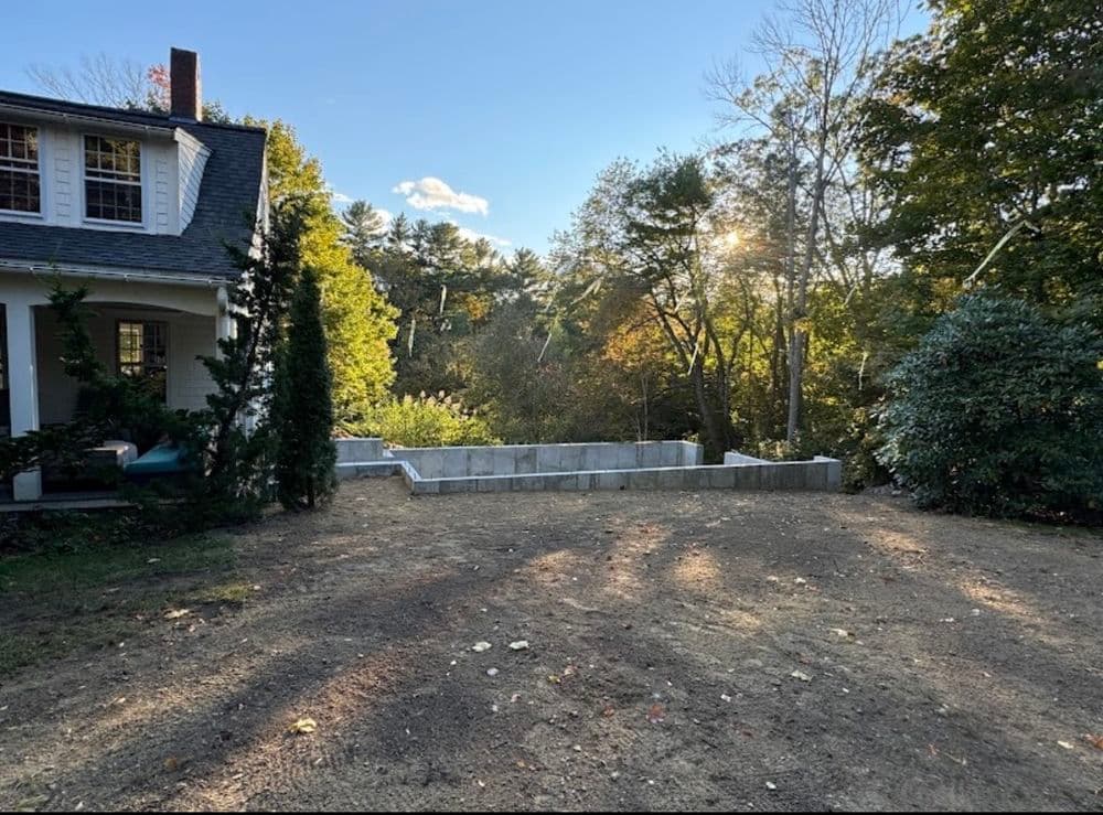 Residential property with newly laid foundation surrounded by trees and sunny landscape.