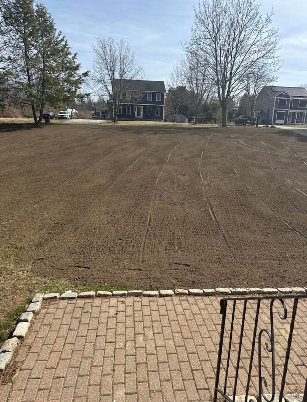 Freshly tilled residential lawn with houses and trees in the background on a sunny day.