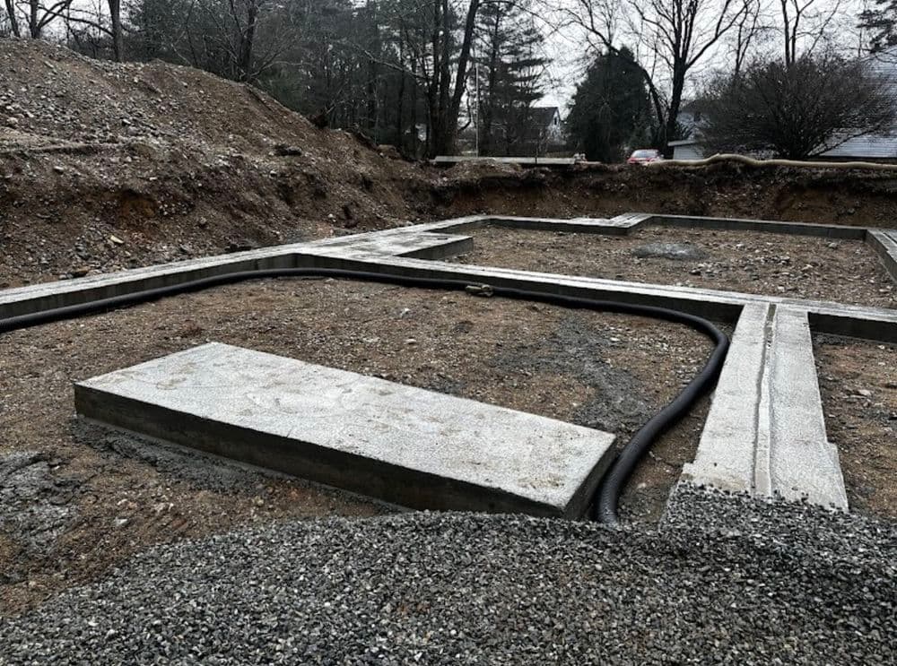 Concrete foundation framework in a gravel excavation site with trees in the background.