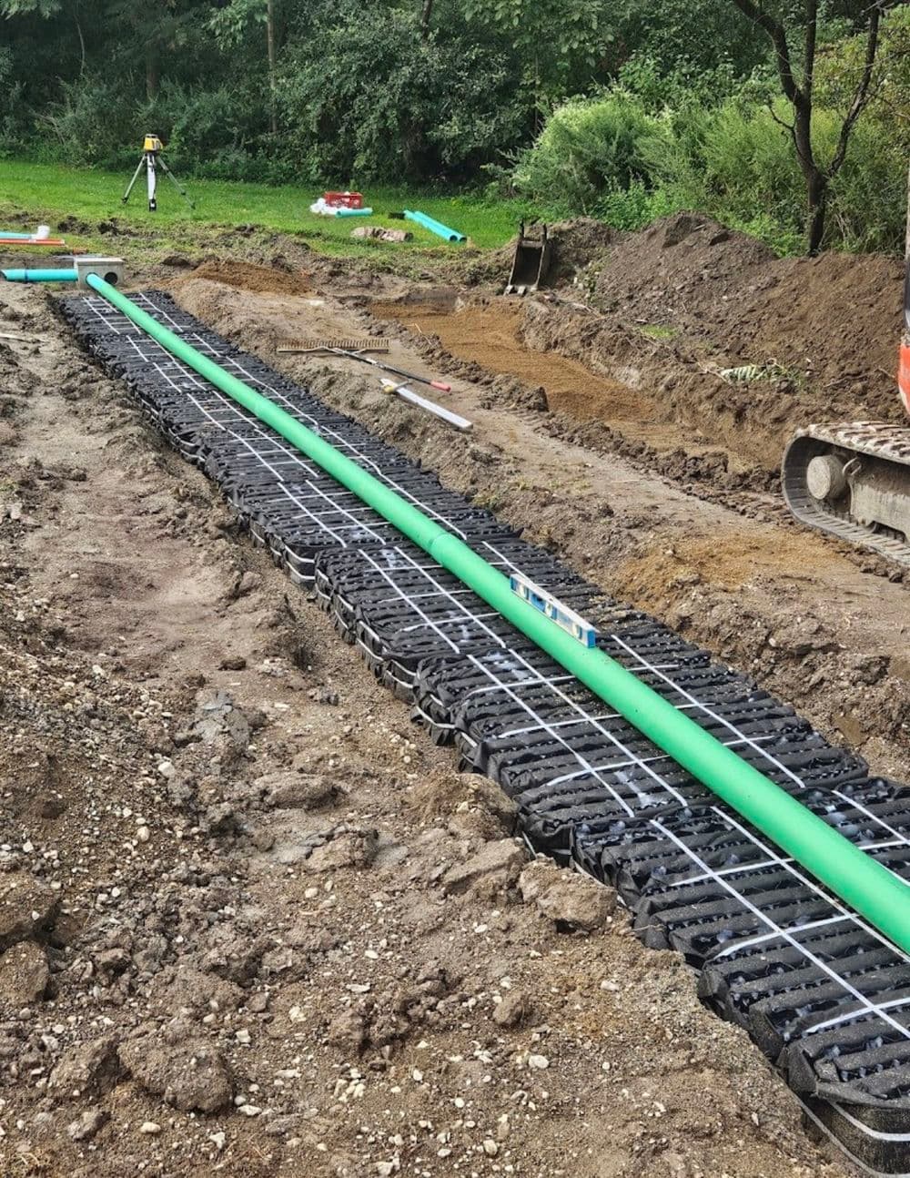 Construction site with a green pipe laid on gravel and soil, surrounded by machinery and tools.