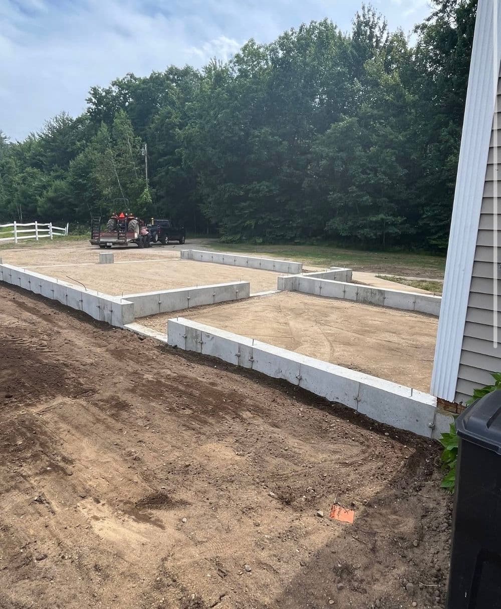 Concrete foundation blocks arranged on a construction site, surrounded by trees and a cleared area.